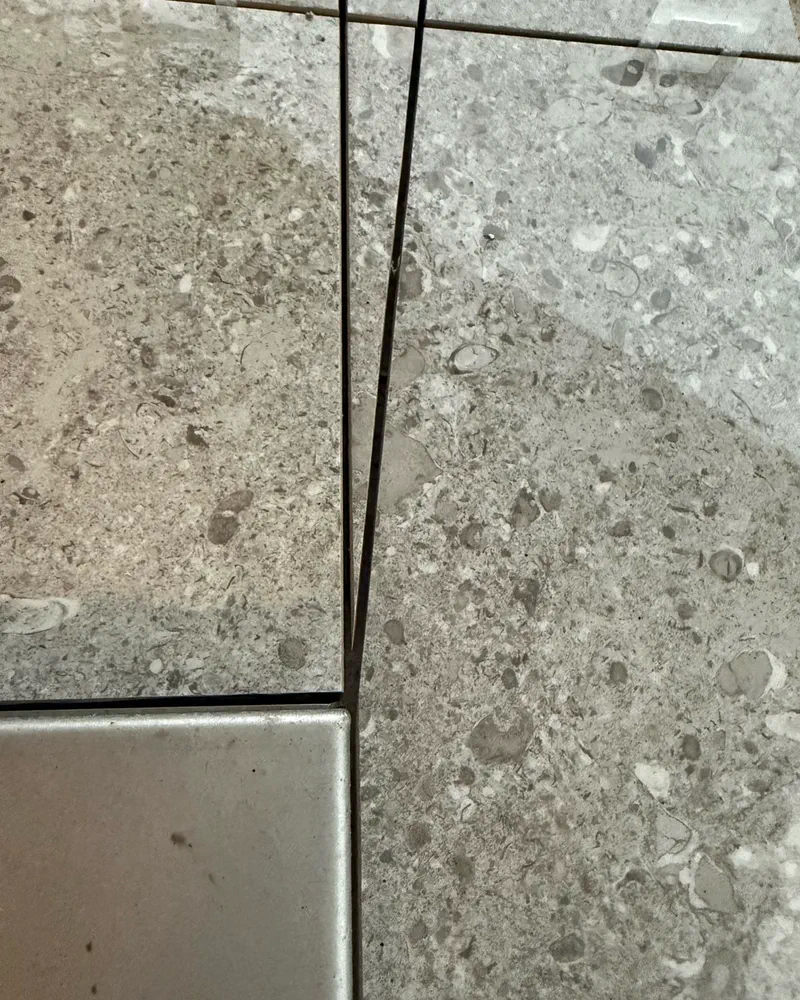 Stone-look tile with hairline joints meeting a metal inlay, by Floors of Glory
